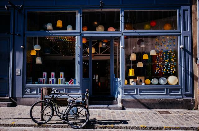 A lit shopfront on a street at dusk with a bicycle parked outside